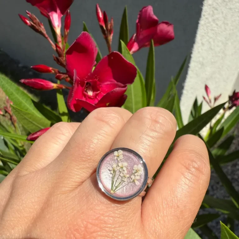 Bague réglable avec inclusion de cerfeuil sauvage blanc sur fond lilas nacré, bijou végétal original porté en extérieur.