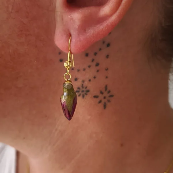 Boucle d’oreille dorée avec véritable bouton de rose séché portée à l’oreille, bijou naturel et romantique en résine fait main.