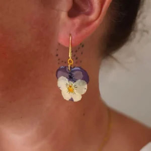 Boucles d’oreilles pendantes en véritables fleurs de pensée violettes et crème portées à l’oreille, monture dorée – bijou floral naturel fait main par L’Atelier d’Emy-Lys