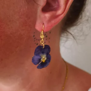 Boucle d’oreille fleur pensée violette naturelle suspendue à un crochet doré, portée à l’oreille – création végétale artisanale
