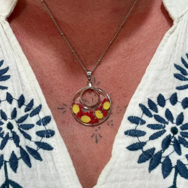 Pendentif floral en résine avec fleurs rouges et pétales jaunes, monté sur chaîne argentée et porté sur buste.