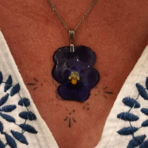 Collier fait main avec pensée naturelle violette, bijou floral en résine porté autour du cou, ambiance artisanale.