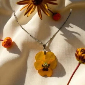 Collier artisanal doré avec une pensée jaune éclatante, fleur naturelle préservée et mise en valeur dans une résine brillante, création unique de L’Atelier d’Emy-Lys.