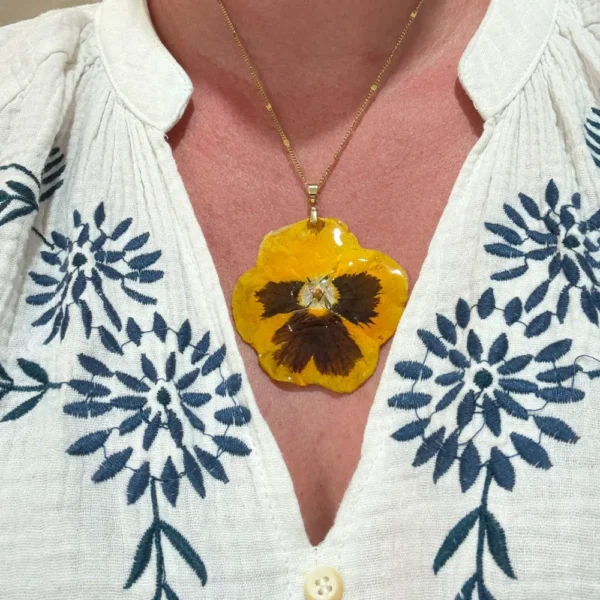 Collier avec grande pensée dorée séchée et montée en résine, porté sur décolleté en blouse blanche – création unique L’Atelier d’Emy‑Lys