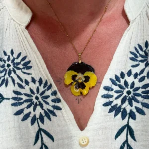 Collier doré avec pensée séchée violet et jaune, bijou floral porté sur haut clair – L’Atelier d’Emy‑Lys