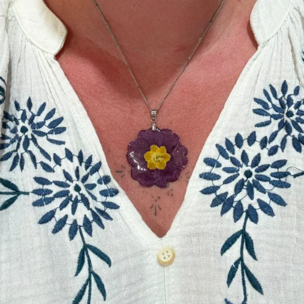 Pendentif en forme de fleur de primevère violette et jaune, monté sur chaîne argentée et porté sur décolleté, bijou naturel fait main par L’Atelier d’Emy-Lys.