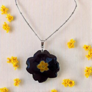 Collier artisanal argenté mettant en valeur une fleur de primevère noire à cœur jaune, bijou élégant inspiré par la nature et la botanique
