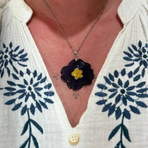 Collier artisanal avec véritable primevère pourpre foncé et cœur jaune, monté sur argenté, porté élégamment, création florale de L’Atelier d’Emy-Lys.