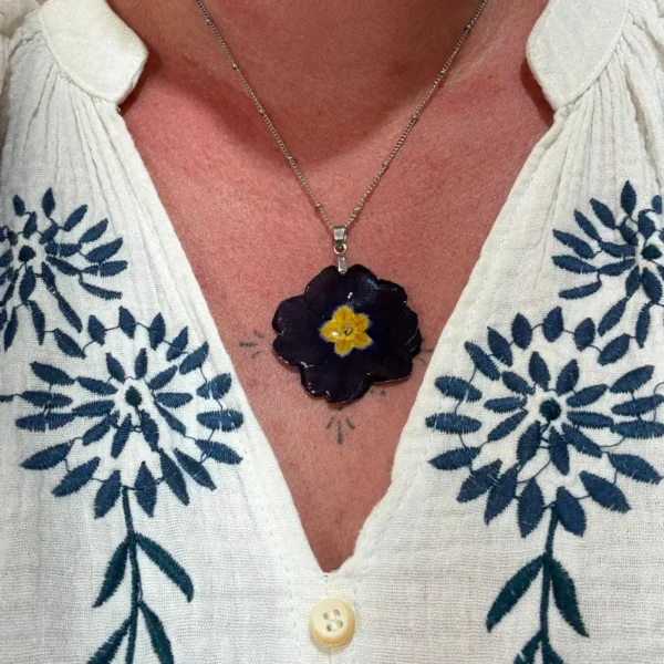 Collier artisanal avec véritable primevère pourpre foncé et cœur jaune, monté sur argenté, porté élégamment, création florale de L’Atelier d’Emy-Lys.