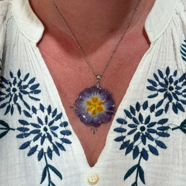 Collier fleuri aux nuances de violet et d’orange, composé d’une véritable primevère séchée, porté sur une peau bronzée.
